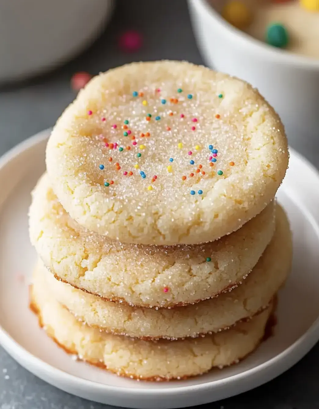 Empilement de quatre biscuits au sucre avec des paillettes colorées sur une assiette blanche.