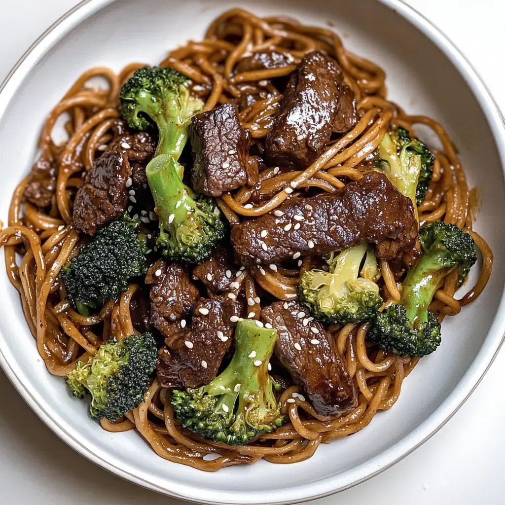 Une assiette de nouilles mélangées avec du boeuf tendre et du brocoli, parsemée de graines de sésame.