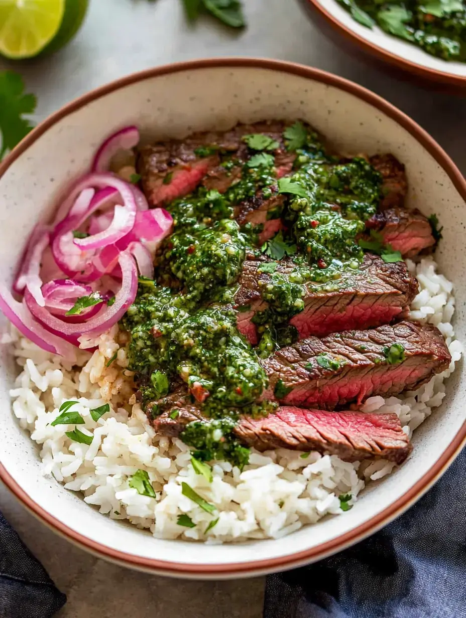 Un bol de riz garni de tranches de bavette, sauce chimichurri, décoré de coriandre et d'oignons rouges.