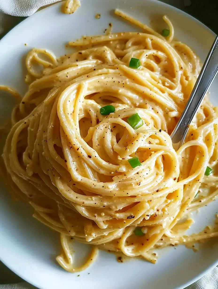 Une assiette de pâtes crémeuses garnies de ciboulette, accompagnée d'une fourchette.