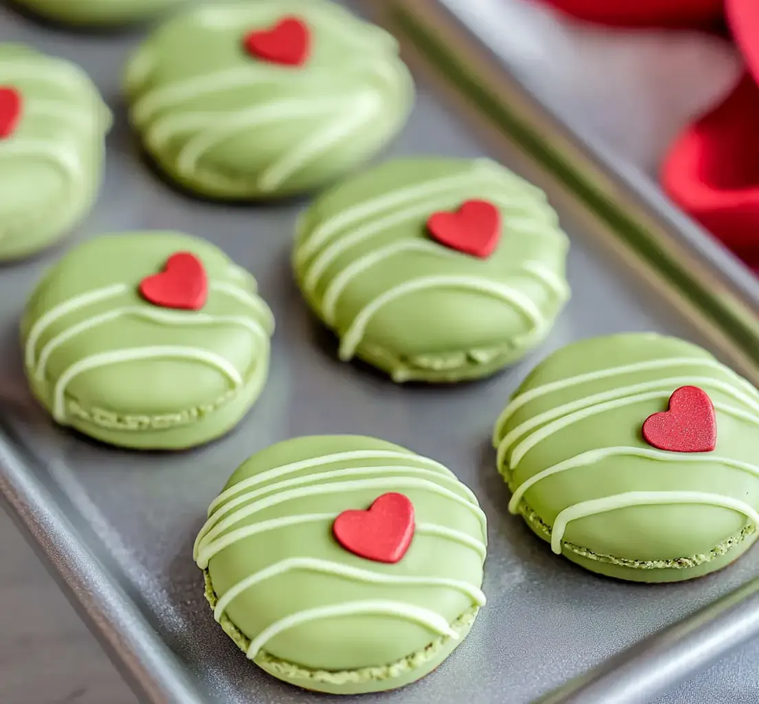 Un plateau de macarons verts décorés avec des cœurs rouges et des filets blancs.